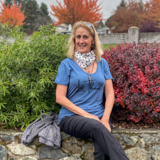 Woman smiling in garden, wearing 'Let Them' shirt.